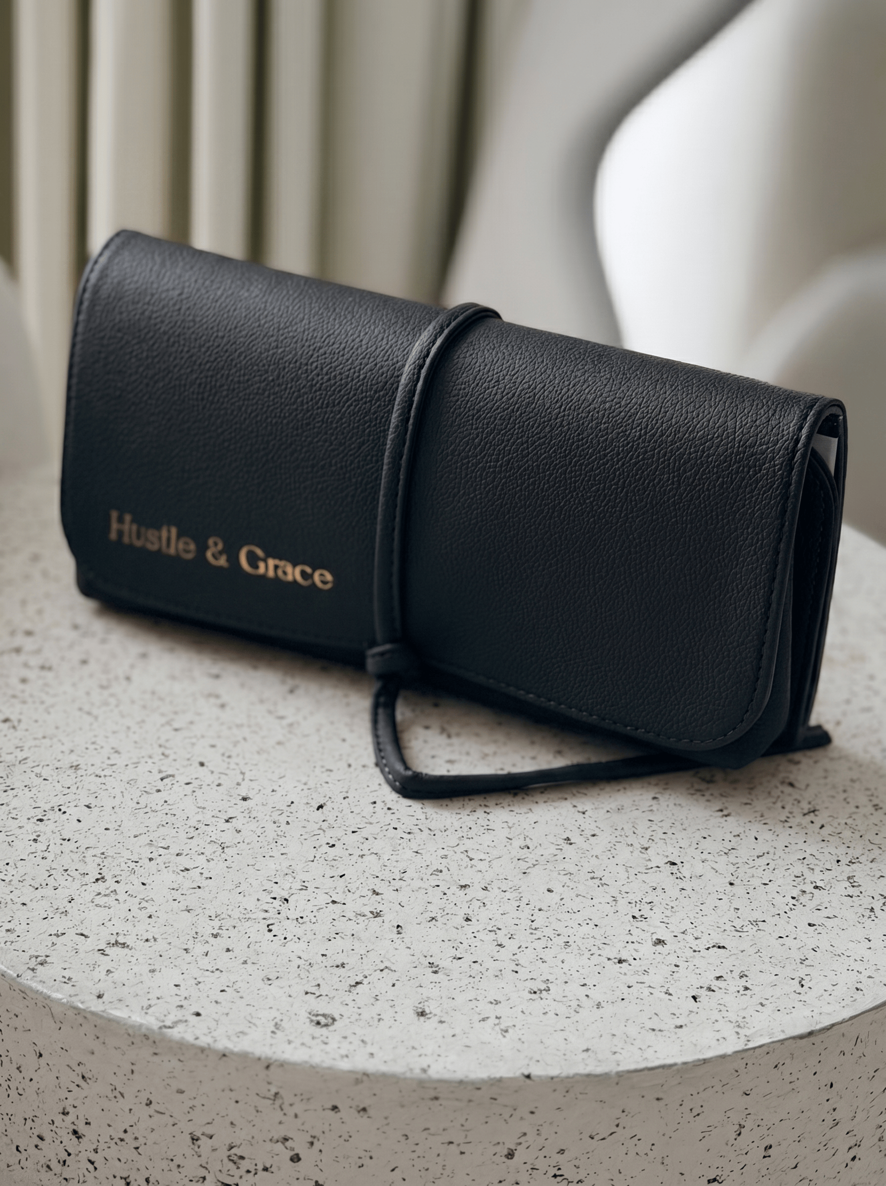 Marli Essentials Pouch in Charcoal with Hustle & Grace branding on a textured surface